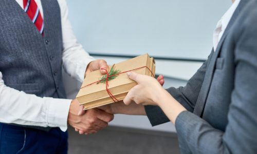 Close up view of unrecognizable businessman shaking hands with female colleague presenting her gift for Boxing Day